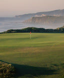 Golf course with a red flag on a green field overlooking a coastal landscape.