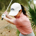 Woman in coral polo swinging a club