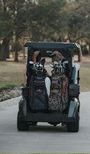 Two golf cart bags in a golf car on a golf course path.