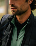 Close-up of a man wearing a black puffer jacket over a light green zip-up performance layer.