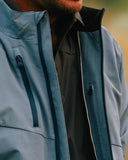 Close-up of a person wearing a light blue softshell jacket with a black inner layer visible at the open collar and front zipper.