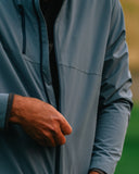 Close-up of a person wearing a slate blue-gray zip-up jacket, with one hand adjusting the zipper. 