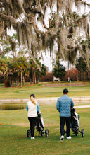 Two people with Sun Mountain golf carts on a golf course with trees and a pond in the background.