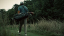 A golfer seen from behind walking along a grassy path carrying a Matchplay Ballistic golf bag with clubs on a golf course.