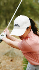 Person playing golf with a white cap and pink shirt