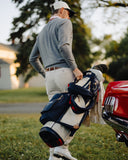 Man with a Hometown golf bag walking towards a red car on a golf course