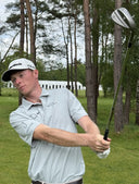 Ryggs Johnston on a golf course swinging a golf club with trees in the background