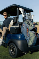 Man sitting in a golf cart with golf bags and clubs on a golf course