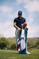 Man holding a golf bag with clubs on a golf course