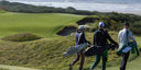Three golfers walking on a golf course with green grass and ocean view.
