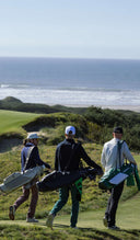 Three golfers walking on a golf course with ocean view