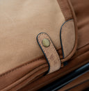 Close-up detail of a brown canvas and leather bag strap with a brass snap button closure.