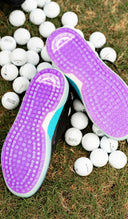 Purple and white athletic shoes with a Sun Mountain logo on grass with golf balls.