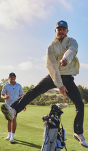 Two golfers on a golf course with one in a yellow jacket and cap, another in a blue shirt and cap.