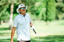 Joel Dahmen in his signature bucket hat, a light blue polo shirt, sunglasses, and a white glove while holding a golf club.