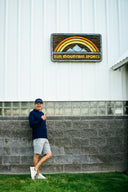 Joel Dahmen in front of Sun Mountain warehouse with a glass block section and a 'Sun Mountain Sports' sign above him.